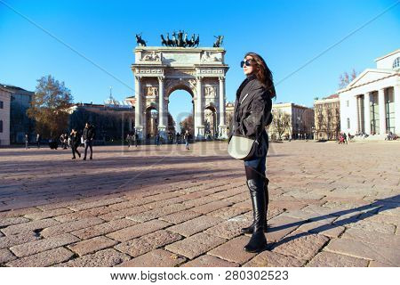 Attractive young woman with long dark hair and sun glasses posing outdoor near Arch of Peace in Milan streets, Italy. Beautiful caucasian model portrait. Steet fashion