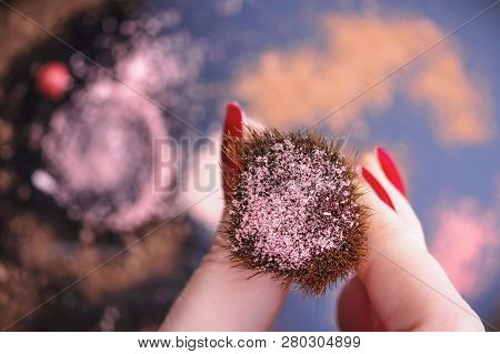 Female Hand Holding Cosmetic Brush With Blushes. Various Crushed Eyes Shadows And Rouge On A Blurred