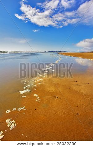 Breda sandstranden och havet skum på sand under utflöde