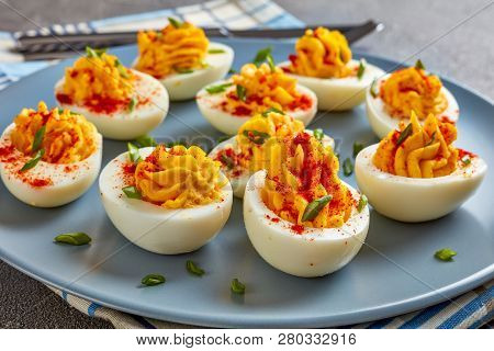 Deviled Eggs Sprinkled With Paprika And Finely Chopped Green Onion On A Grey Plate On A Concrete Tab