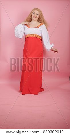 beautiful chubby caucasian blonde girl in red and white national Russian sundress on solid pink back