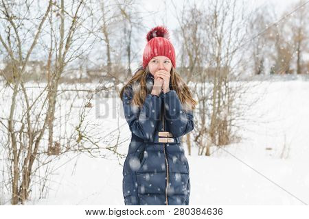 Young Beautiful Fair-haired Girl Breathes On Her Hands In Order To Warm Them In The Park Under Soft 