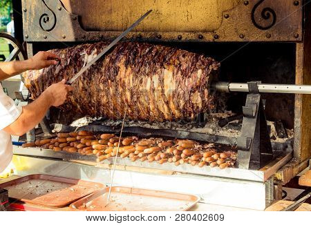 Chef Dressed In Red Cutting Turkish Cag Kebab In Display