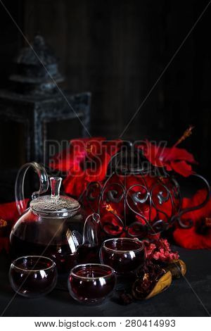 Herbal Hibiscus Tea Carcade With Red Hibiscus Flowers. Dark Mood Photo.