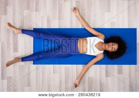 Athletic Young Woman Lying On Blue Yoga Mat Over The Hardwood Floor