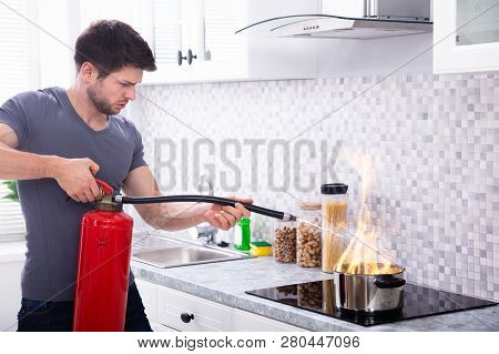 Man Using Fire Extinguisher To Stop Fire On Burning Cooking Pot In The Kitchen
