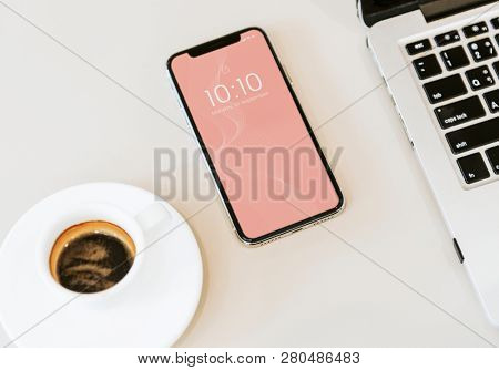 Phone mockup on white table with a laptop and a coffee cup