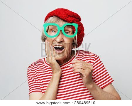 lifestyle, people and party concept: funny grandmother wearing red clothes holding falce glasses and  ready for party
