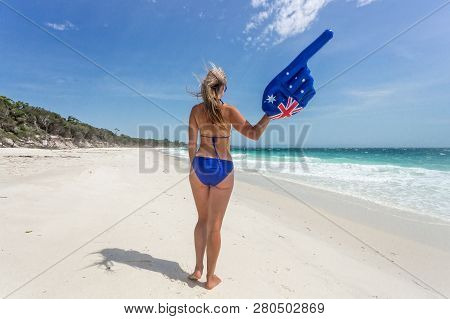 A Woman On The Beach In Bikini With Wind Swept Hair Has An Inflateable Large Hand Pointing Finger To