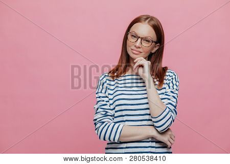Studio Shot Of Attractive Woman With Brown Hair, Crosses Hand Over Chest, Keeps Hand Under Chin, Foc