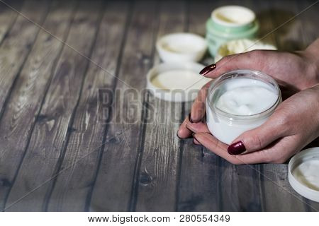 A Young Woman Is Holding A Jar Of Cream. Manicure With Red Lacquer. On The Table Are Open Jars Of Cr