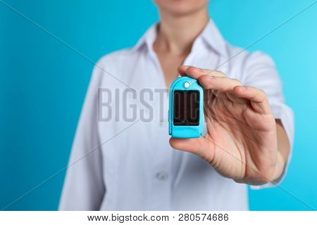 Female Doctor Holding Pulsimeter On Color Background, Closeup. Medical Object