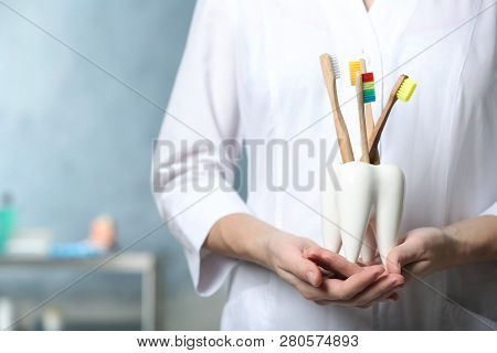 Dentist With Wooden Toothbrushes In Ceramic Holder On Blurred Background, Closeup View. Space For Te