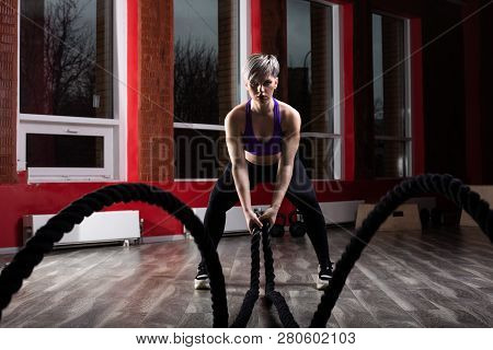 Fit And Muscular Woman Exercising With Battling Ropes At Fitness Studio. Female Athlete Doing Battle