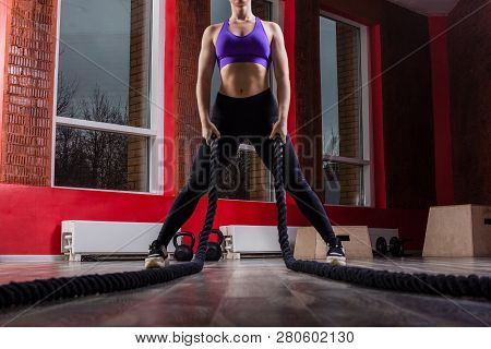 Fit And Muscular Woman Exercising With Battling Ropes At Fitness Studio. Female Athlete Doing Battle