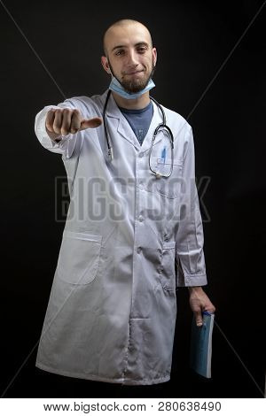 Young Male Doctor Holding A File, Having Stethoscope And Mask Displaing A Finger Thumb Horizontally.