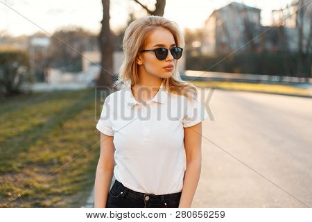 Young Attractive Hipster Woman In Stylish Sunglasses In A White Polo T-shirt In Black Jeans Walking