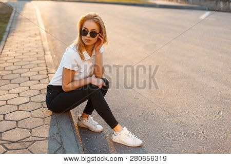 Young Beautiful Stylish Hipster Woman With Sunglasses In A White Polo Shirt And Black Jeans With Sne