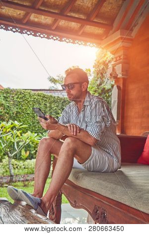 Man Using Smart Phone On A Terrace Sofa In Summertime.