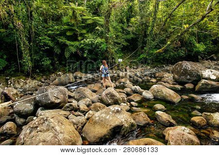 Young Woman Crossing Stream On A Trail To Middle Tavoro Waterfalls In Bouma National Heritage Park O