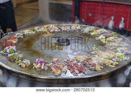 Cooking Street Food On A Large Firebox. Frying Meat And Seafood On The Brazier In The Street. A Cook