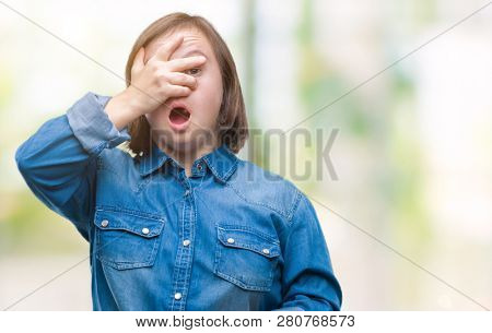 Young adult woman with down syndrome over isolated background peeking in shock covering face and eyes with hand, looking through fingers with embarrassed expression.