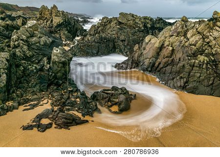 Slow Shutter Speed Was Used To Capture This Image Of A Wave Swirling Though The Rocks On The Beach. 