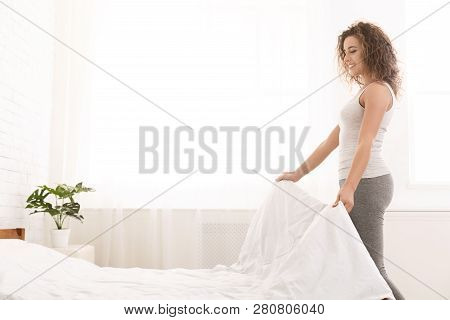 Young Woman Making Bed And Organizing Room In Morning, Copy Space