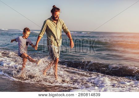 Happy Father And Son, Man & Boy Child, Running And Having Fun In The Sand And Waves Of A Sunny Beach