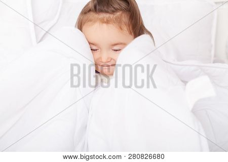 Portrait Of Baby Girl Lying In Bed Under Featherbed