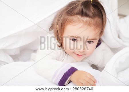 Portrait Of Baby Girl Lying In Bed Under Featherbed