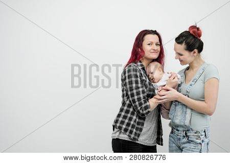 Two Young Women With A Baby On A White Background. Same-sex Marriage And Adoption, Homosexual Lesbia
