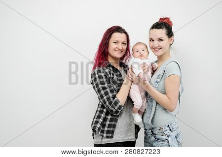 Two Young Women With A Baby On A White Background. Same-sex Marriage And Adoption, Homosexual Lesbia