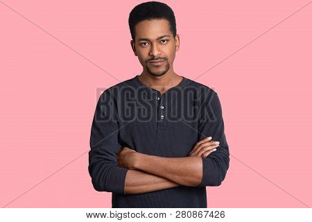 Indoor Shot Of Self Confident Serious Black Man Keeps Arms Folded, Has Little Beard, Tries Make Deci