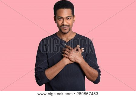 Horizontal Shot Of Impressed Touched Man Holds Hands On Chest, Expresses Thankfullness, Hears Heart 