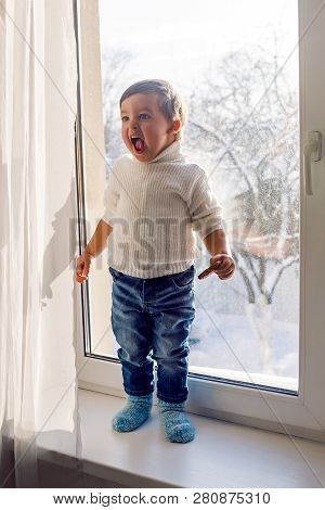 Boy In A White Sweater Standing At The Window On The Windowsill