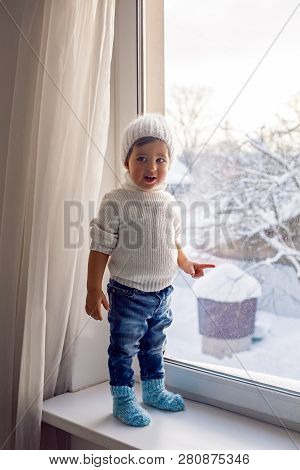 Boy In A White Sweater Standing At The Window On The Windowsill
