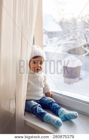Boy In A White Sweater Standing At The Window On The Windowsill