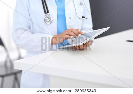 Close-up Of Female Physician Using Digital Tablet  While Standing Near Reception Desk At Clinic Or E