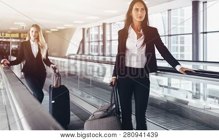 Two Confident Women Wearing Formal Suits Standing On Moving Walkway In Airport