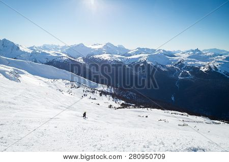Snowboarder On A Hill At The Top Of Blackcomb, 7th Heaven, With A View Looking Toward Whistler On A 