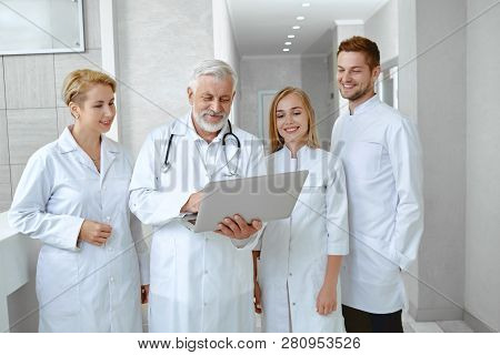 Portrait Of Four People Standing In White Unifotm In Hospital. Concilium Of Men And Women Working Ta