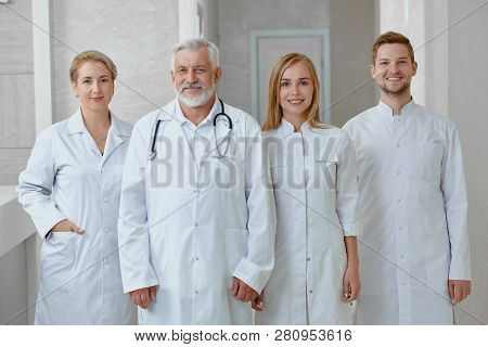 Front View Of Doctors In White Uniform Of Different Age. Cheerful Smiling Professional Medical Worke