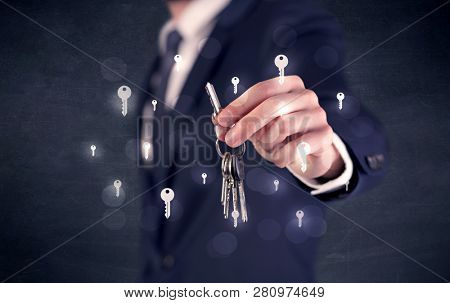 Businessman in suit holding keys with keys graphics around and dark background