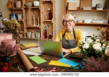 Portrait Of Smiling Female Small Business Owner Using Laptop And Looking At Camera In Flower Shop, C