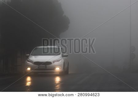 Adrano, Catania Italy - 01 18 2019: A White Car With Yellow Lights On The Wet Road In The Fog