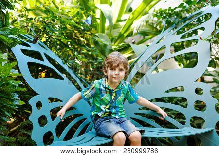 Little Blond Preschool Kid Boy Discovering Flowers And Butterflies At Botanic Garden. Schoolchild In