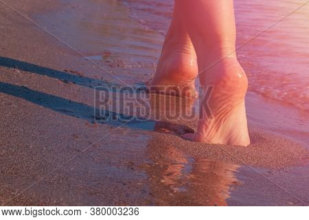 Barefoot Woman Legs Are Walking Along Seaside On Sandy Beach At Rising Sun Sunlbeams. Summer Vacatio