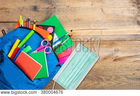 School, Coronavirus Days. School Supplies And Medical Protective Face Mask Out Of A Backbag, Wooden 