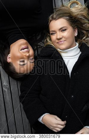 Smiling Friends Lying On Bench Together In City
